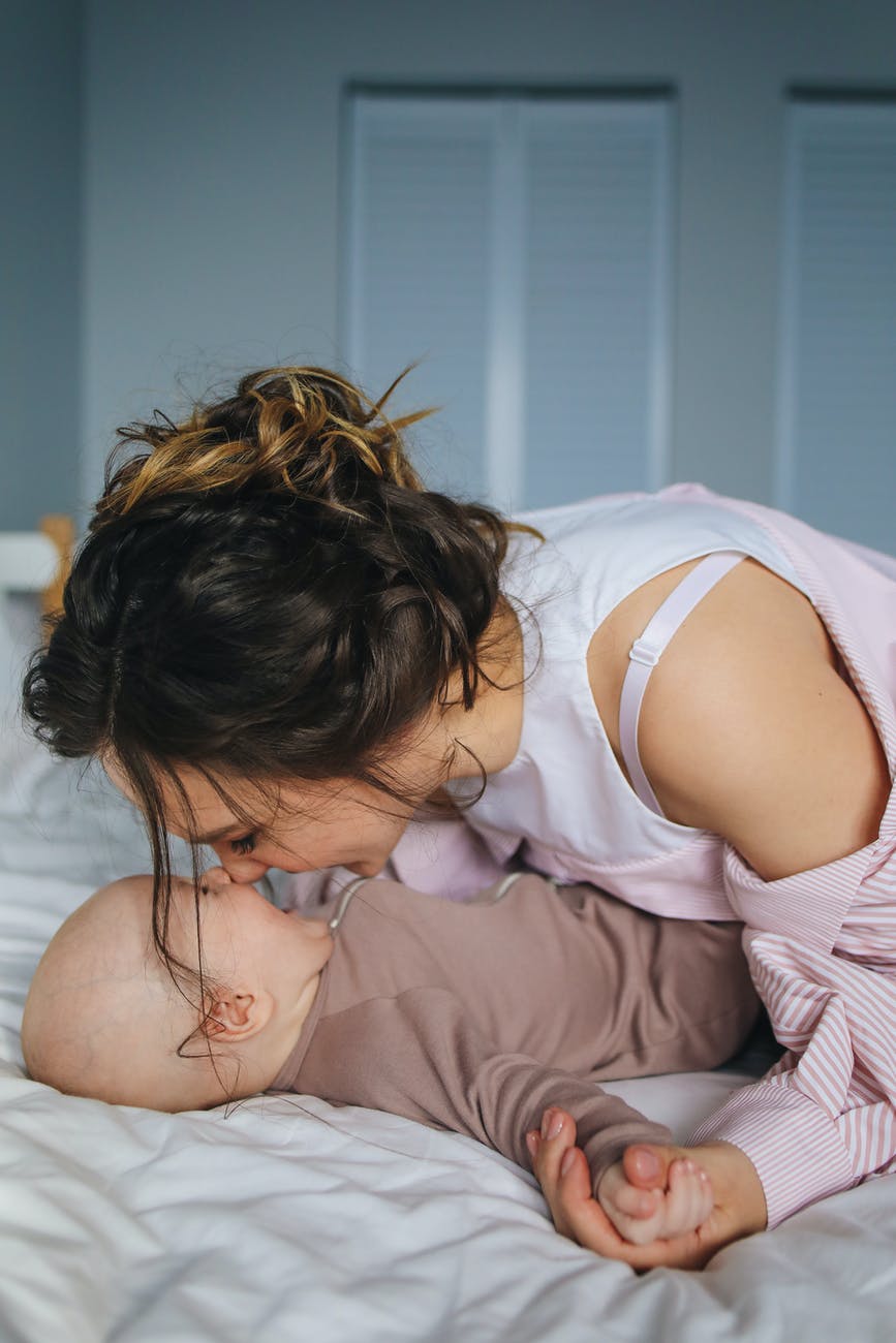 woman in white and pink striped long sleeve shirt playing with baby lying on bed