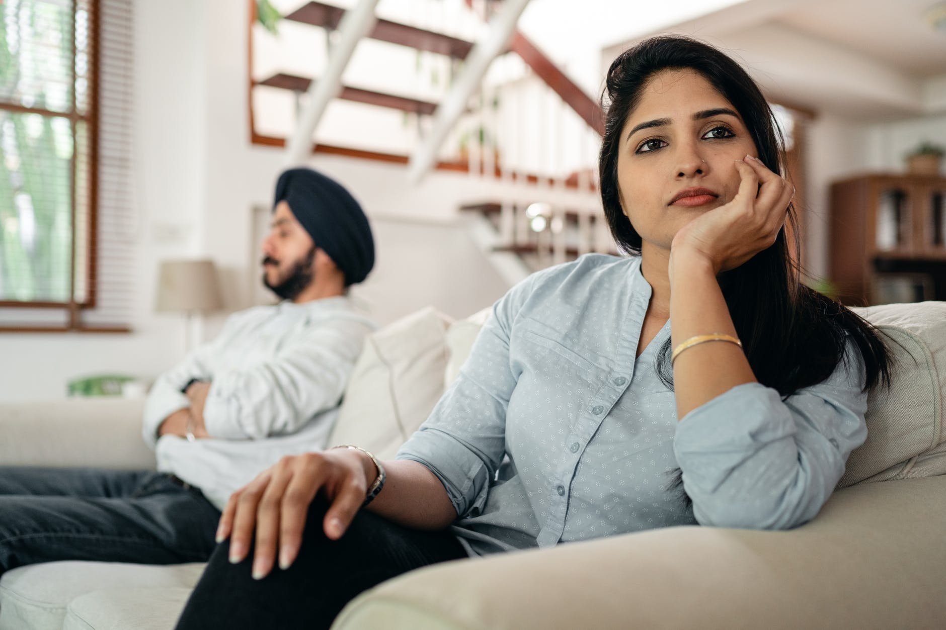 sad young indian woman avoiding talking to husband while sitting on sofa