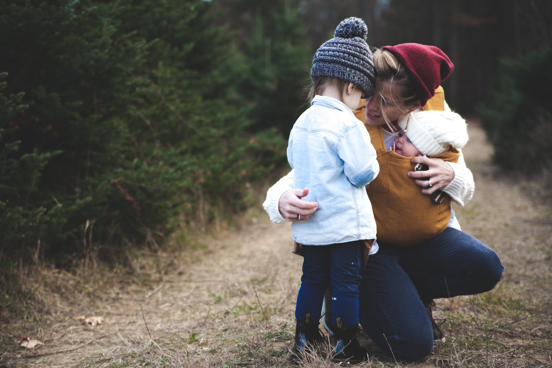 woman with brown baby carrier and little kid in white jacket